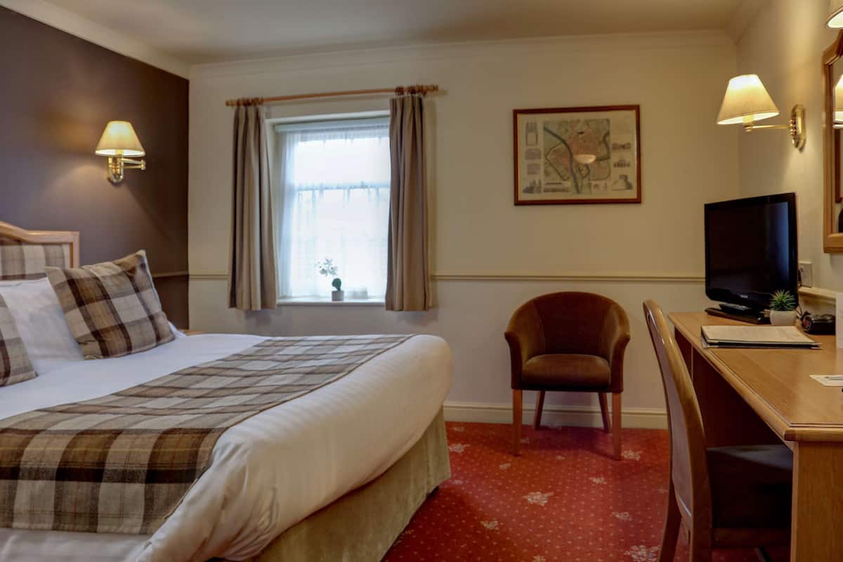 Une chambre d’hôtel équipée d’un lit, d’un bureau, d’une chaise, d’une télévision et d’une fenêtre avec des rideaux.