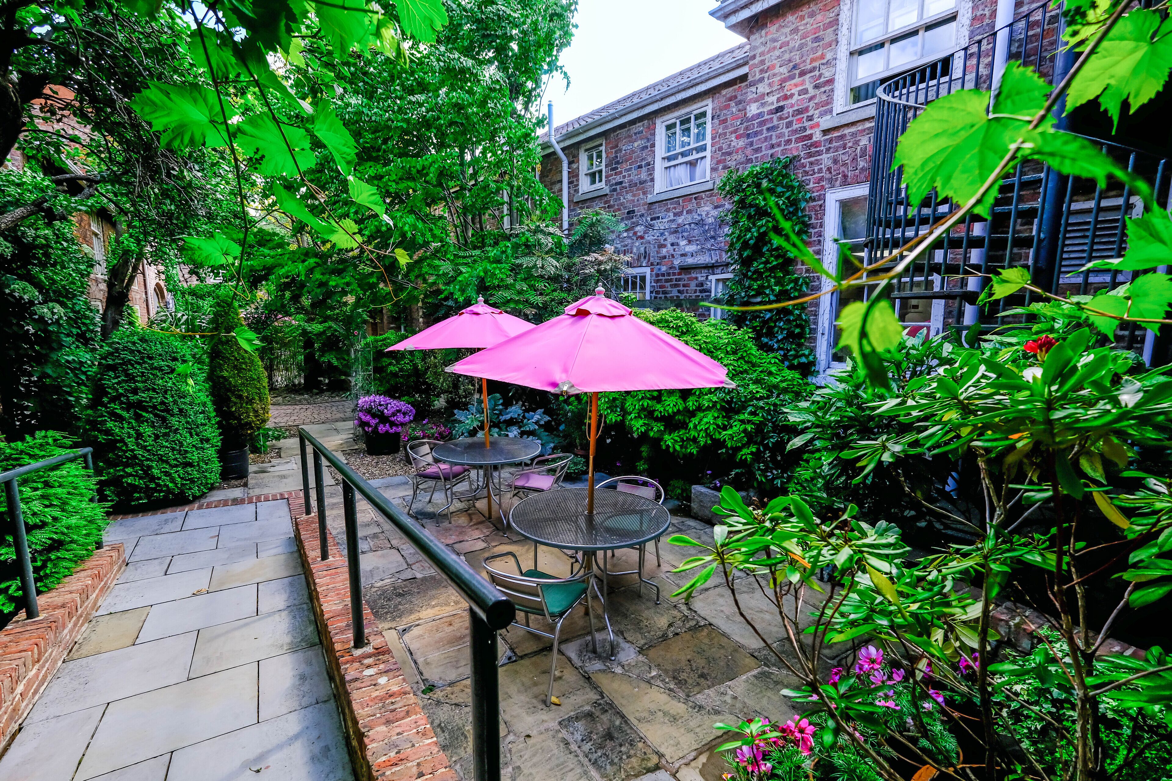 Ein Innenhof mit Steintreppen, Metallgeländern und Gartenmöbeln mit rosa Sonnenschirmen.
