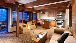 A spacious living area with a sofa, armchairs, a coffee table with a laptop, a kitchen with modern appliances, and large windows offering a view.