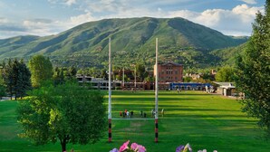 A grassy field with a sports field, a building, and mountains in the background.