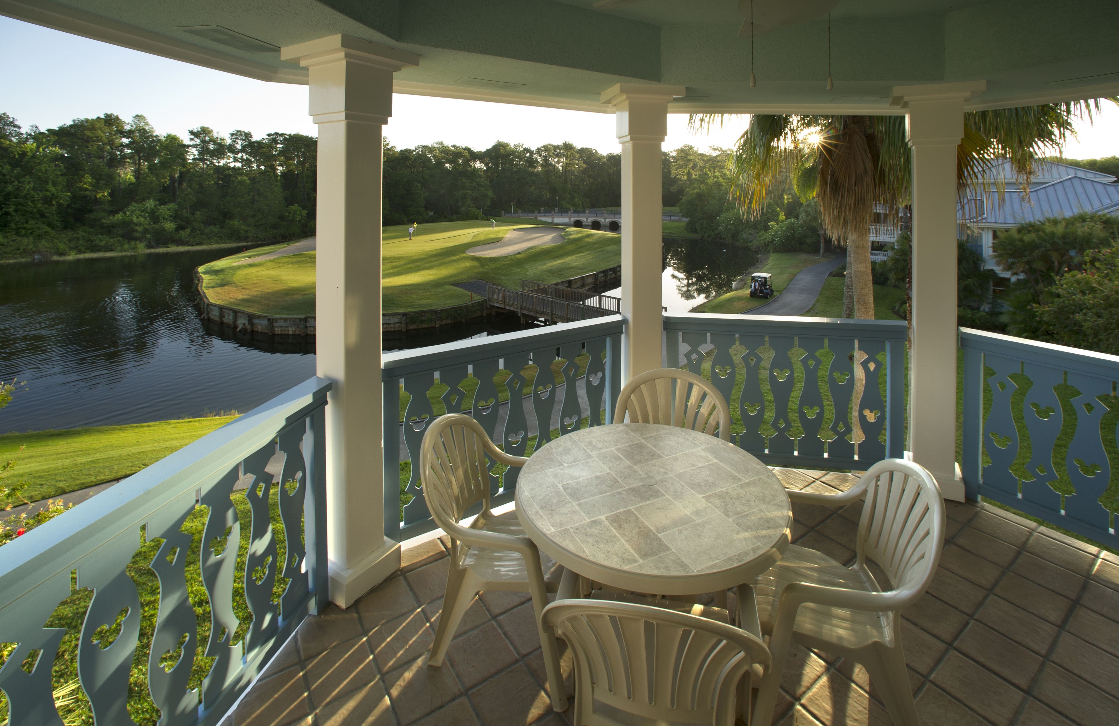 Eine überdachte Terrasse mit Tisch und Stühlen, mit Blick auf einen Golfplatz und ein Gewässer.