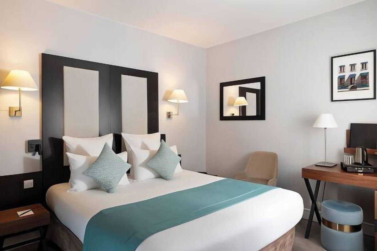 A hotel room with a large bed, two wall-mounted lamps, a desk with a chair, and a framed picture on the wall.
