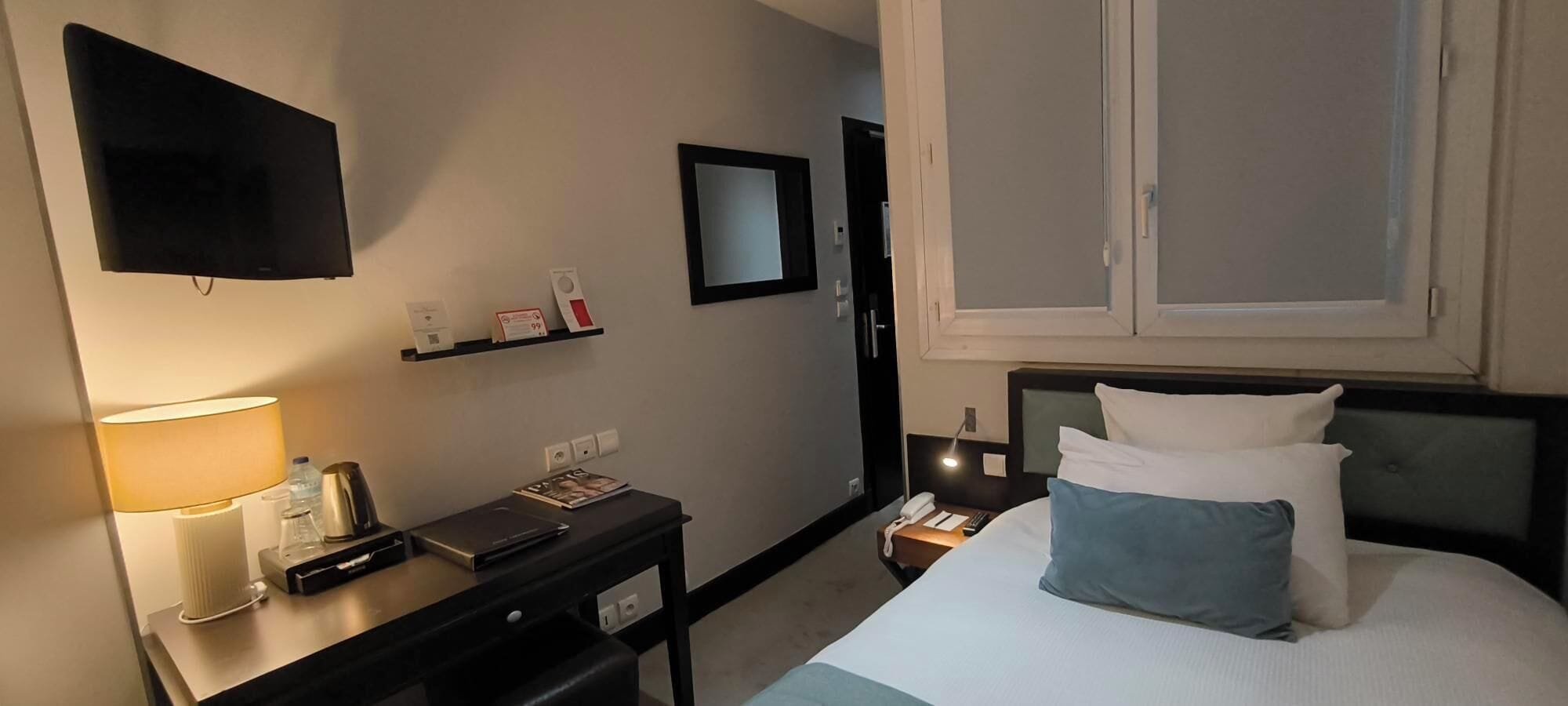 A hotel room with a bed, bedside table, lamp, and a flat-screen TV mounted on the wall.