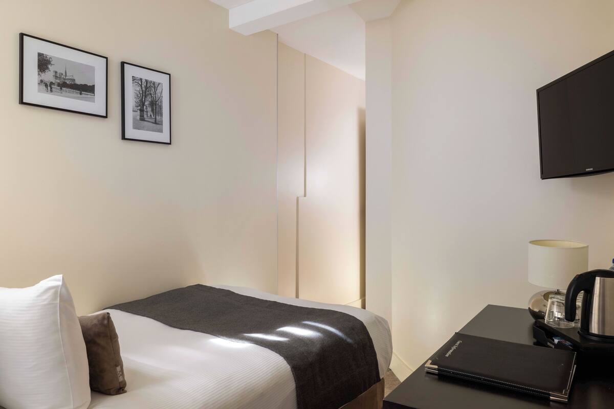 A hotel room with a bed, a desk with a lamp, a flat-screen TV, and two framed pictures on the wall.