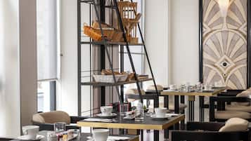 Uma sala de jantar moderna com mesas preparadas para o café da manhã, cestos de vime em uma estante de metal e um painel decorativo na parede.