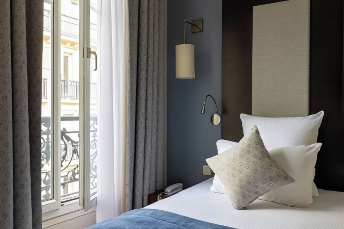 Une chambre d’hôtel avec un lit, une table de chevet, une lampe et une vue sur un balcon.