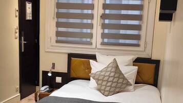Una habitación de hotel con una cama, dos lámparas de noche, un teléfono, una ventana con persianas y una puerta.