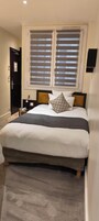 A neatly made bed with a grey and white duvet, two bedside tables with lamps, and a window with blinds.