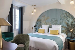 Une chambre d’hôtel avec un grand lit, un fauteuil vert, une table ronde et une lampe.