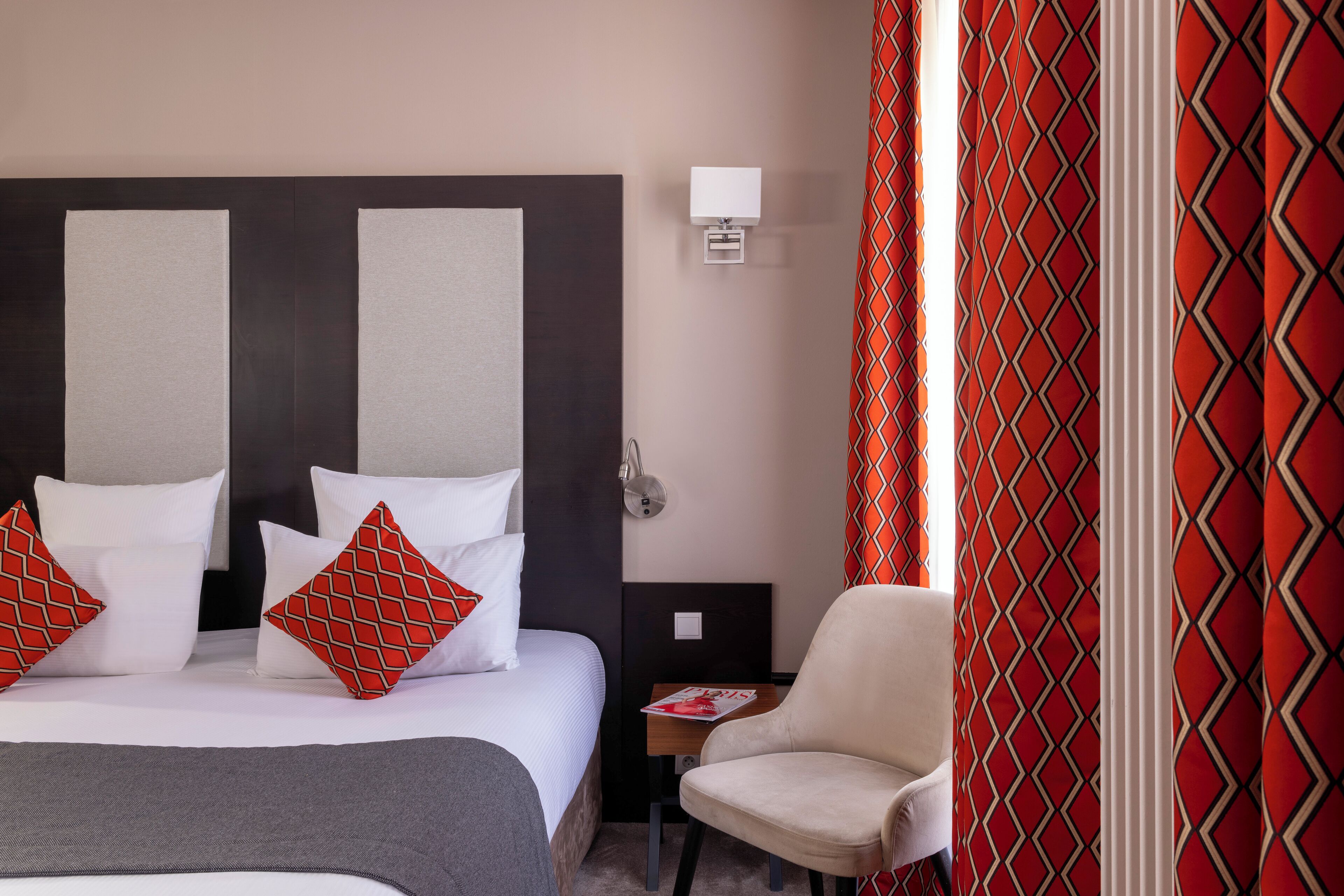 Una habitación de hotel con una cama, una mesita de noche, una silla y una cortina estampada.