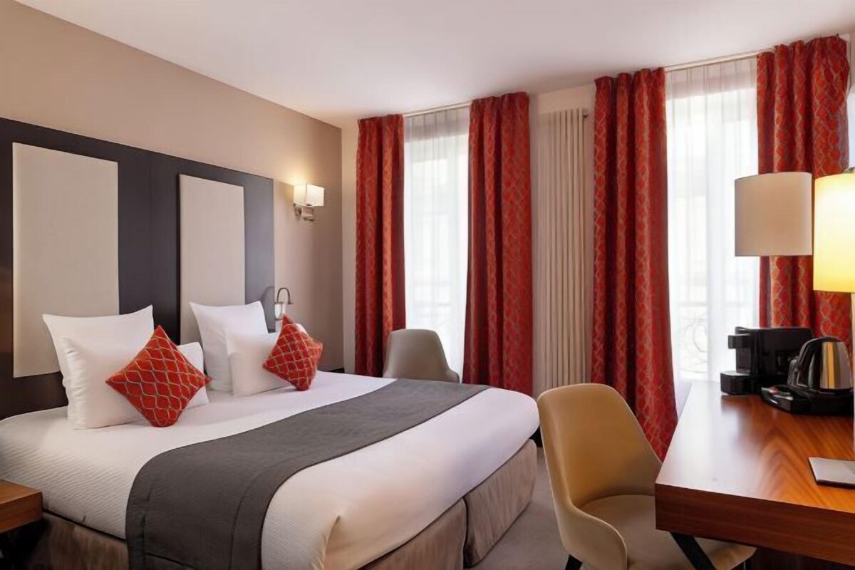 A hotel room with a bed, a desk, a chair, a lamp, and a coffee maker.