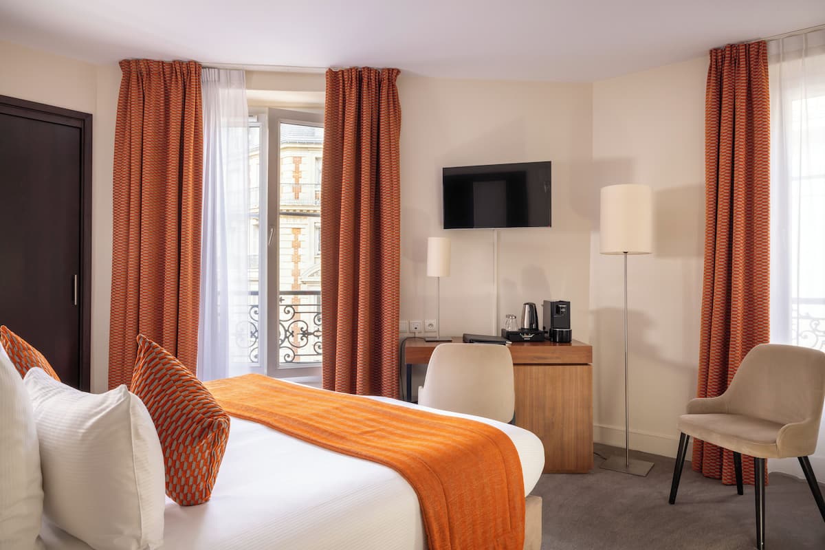 A hotel room with a bed, a desk, a chair, a TV, and a window with curtains.