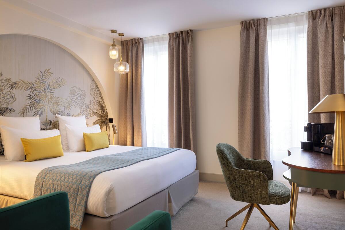 A hotel room with a large bed, a desk with a lamp, and a chair.
