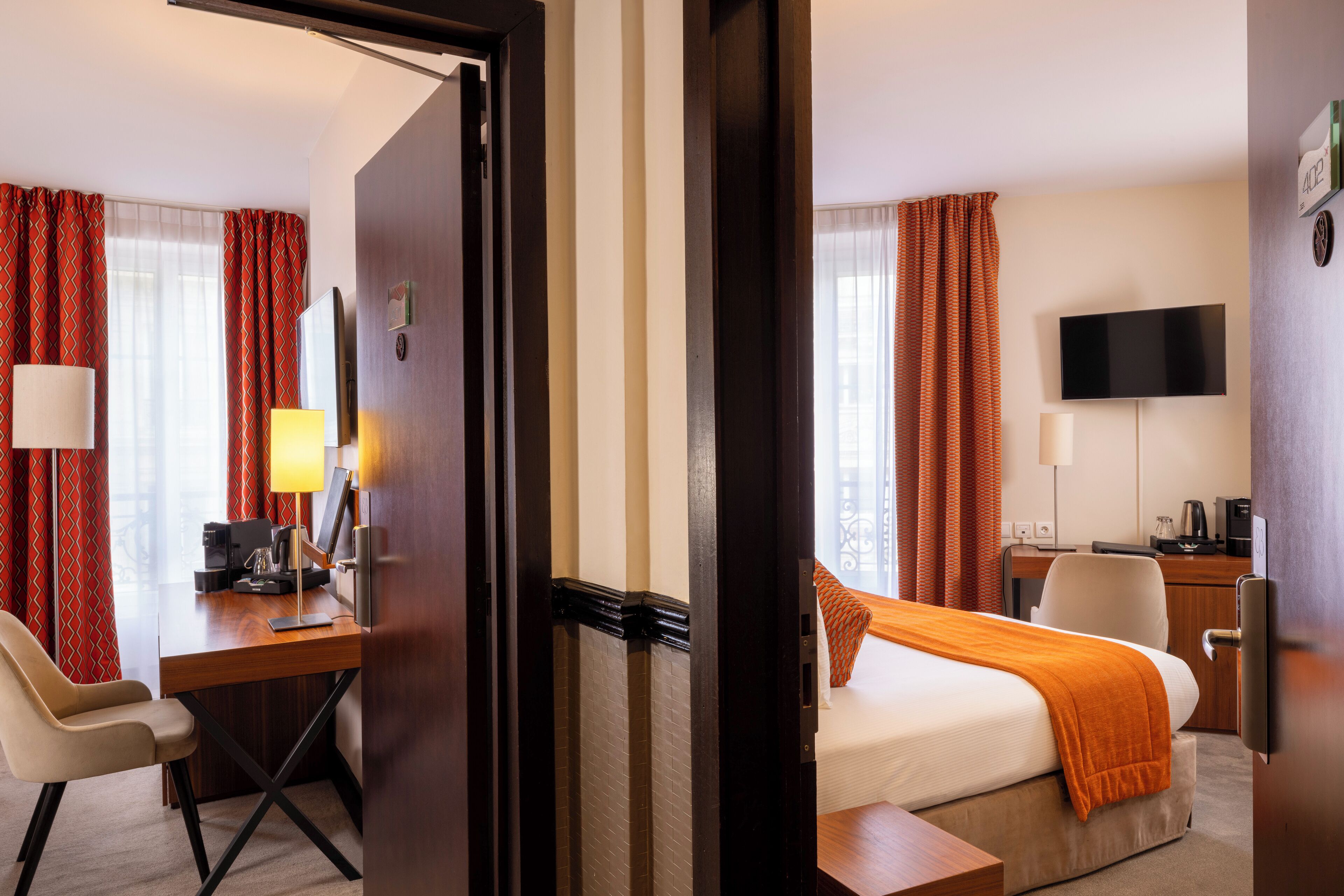 Habitación de hotel con cama, escritorio, silla, televisor y ventana con cortinas.