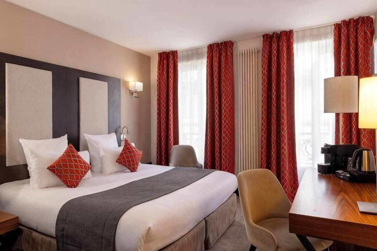 A hotel room with a bed, a desk, a chair, and a lamp.
