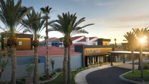 A modern hotel entrance with a covered driveway, palm trees, and a clear sky. - Courtyard by Marriott Phoenix Mesa (Mesa)