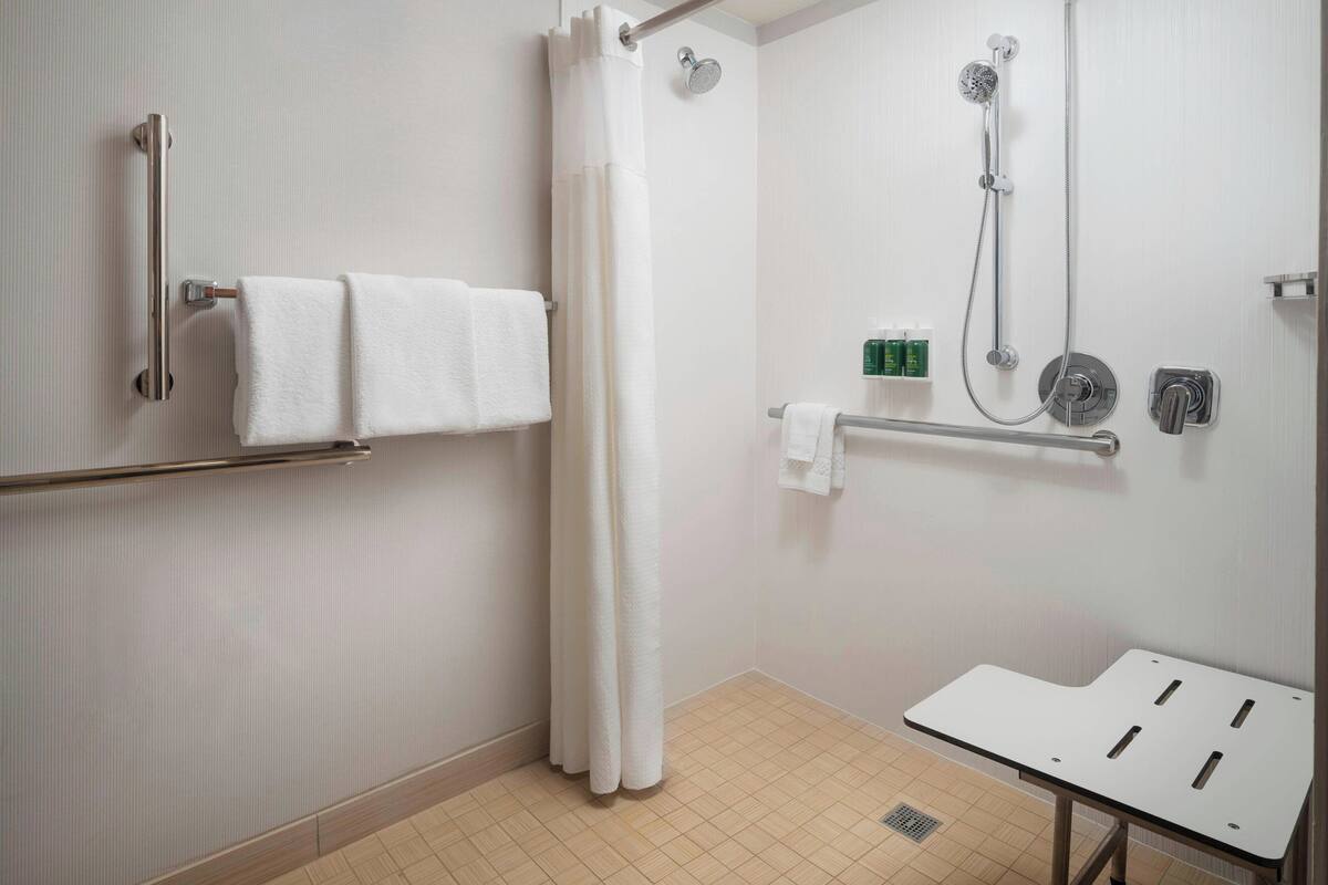 Un baño con ducha, barras de apoyo, un lavamanos blanco y un perchero para toallas.