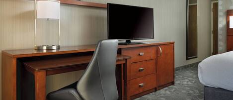 Een hotelkamer met een houten bureau, een televisie, een stoel, een dressoir en een bed.