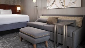 A modern hotel room with a large bed, a sofa, an ottoman, a side table, and a floor lamp. - Courtyard by Marriott Phoenix Mesa (Mesa)