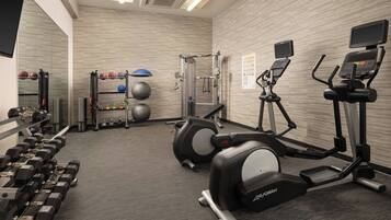 Une salle de sport équipée de machines d’exercice, d’haltères et d’un miroir.