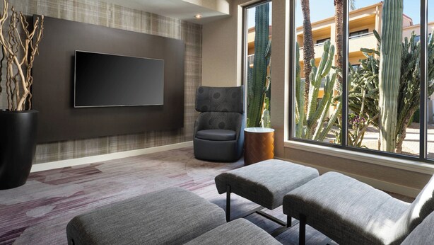 A modern room with a flat-screen TV, a comfortable chair, a sofa, and a large window with a view of cacti and a building. - Courtyard by Marriott Phoenix Mesa (Mesa)
