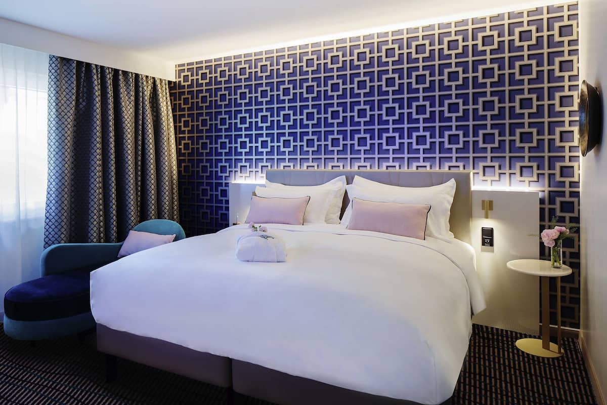 A modern hotel room with a large bed, a small round table, and a chair.