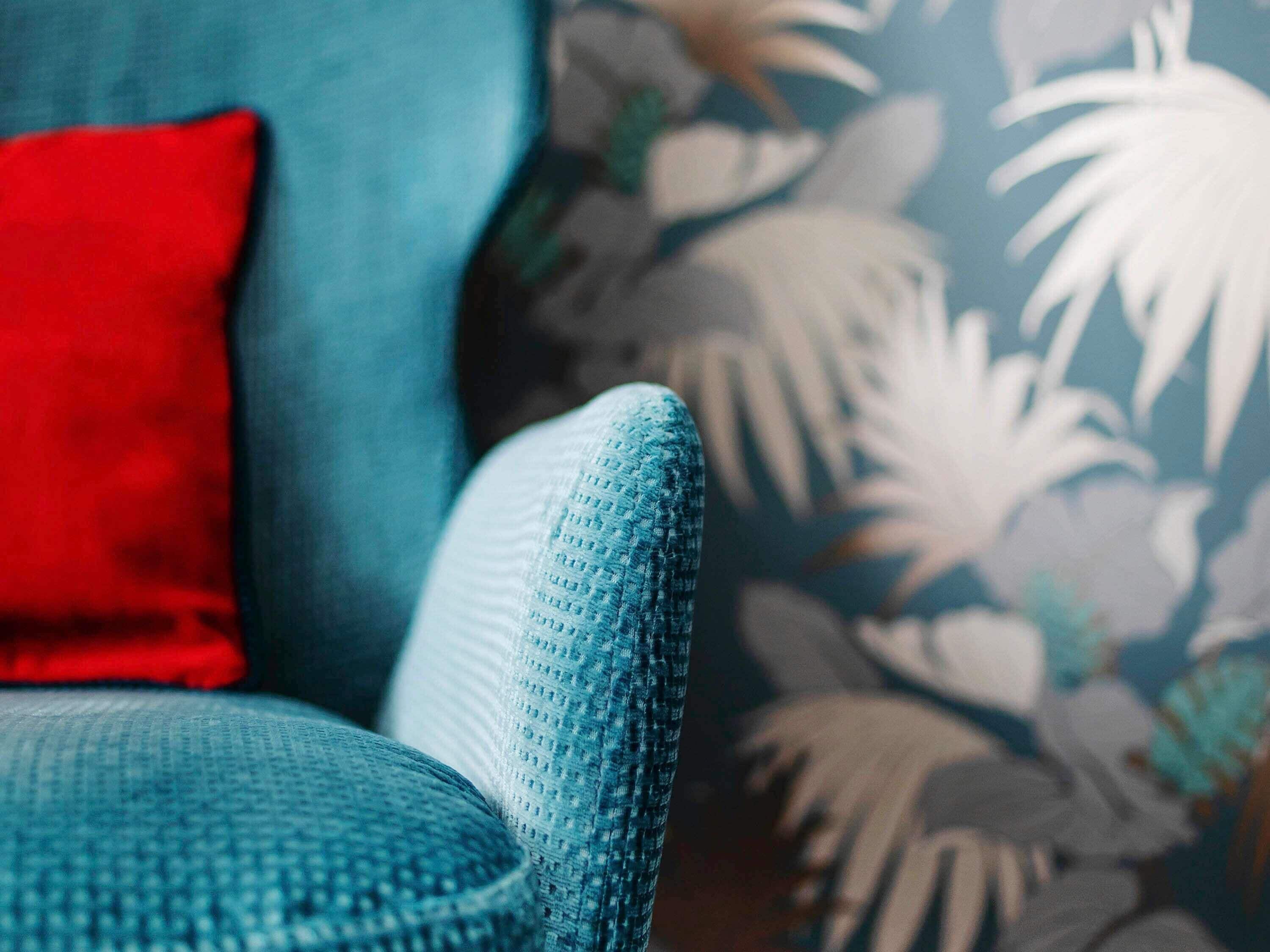 Ein Detailaufnahme eines hölzern-grünen Sofas mit strukturierter Stoffoberfläche und einem roten Kissen.
