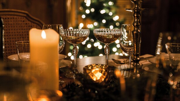 Une table dressée avec des verres en cristal, une bougie et un sapin de Noël en arrière-plan.