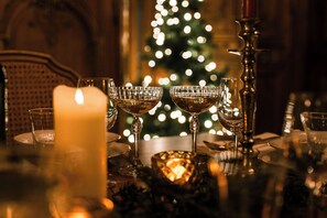 A table set with crystal glasses, a candle, and a Christmas tree in the background.