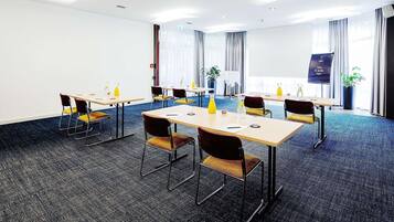 Een vergaderzaal met tafels, stoelen en een projectiescherm.