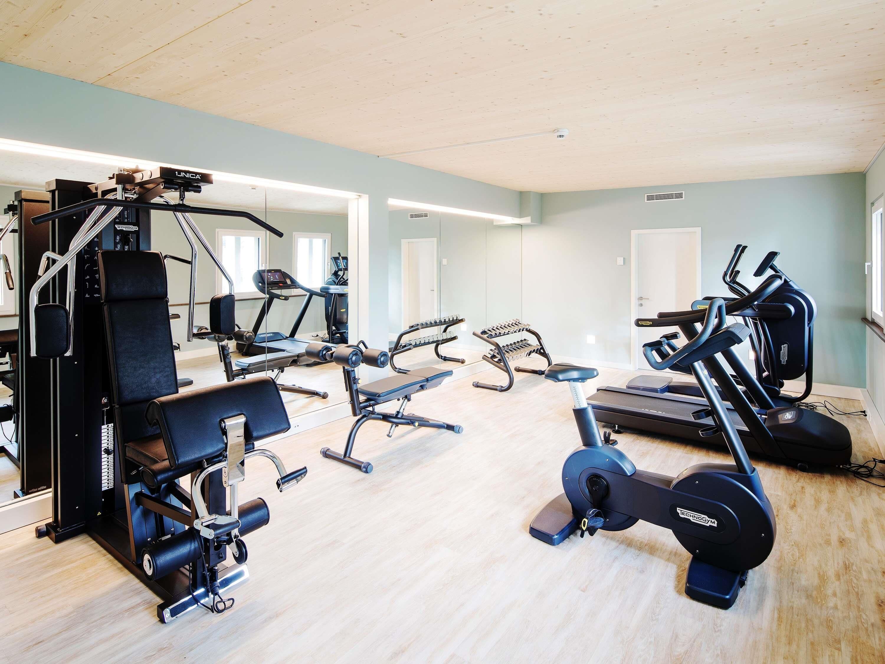 Un gimnasio con equipo de ejercicio variado, incluyendo cintas de correr, un banco de pesas y una máquina de remo.