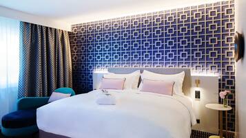 A modern hotel room with a large bed, a bedside table, a wall-mounted lamp, and a patterned wall.