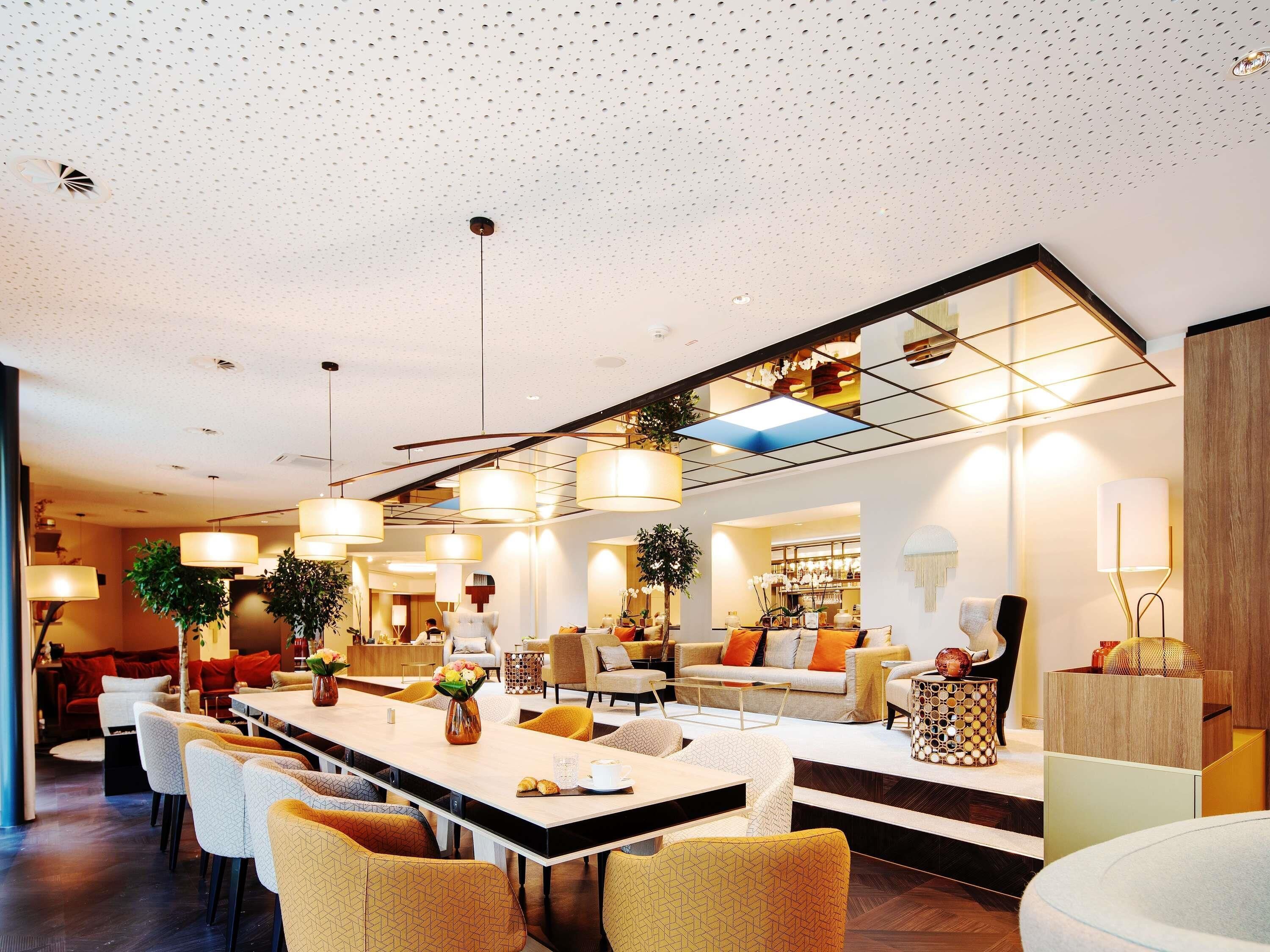 Eine moderne Hotelhalle mit einer langen Rezeption, mehreren Sitzbereichen und einem großen Spiegel, der den Raum widerspiegelt.