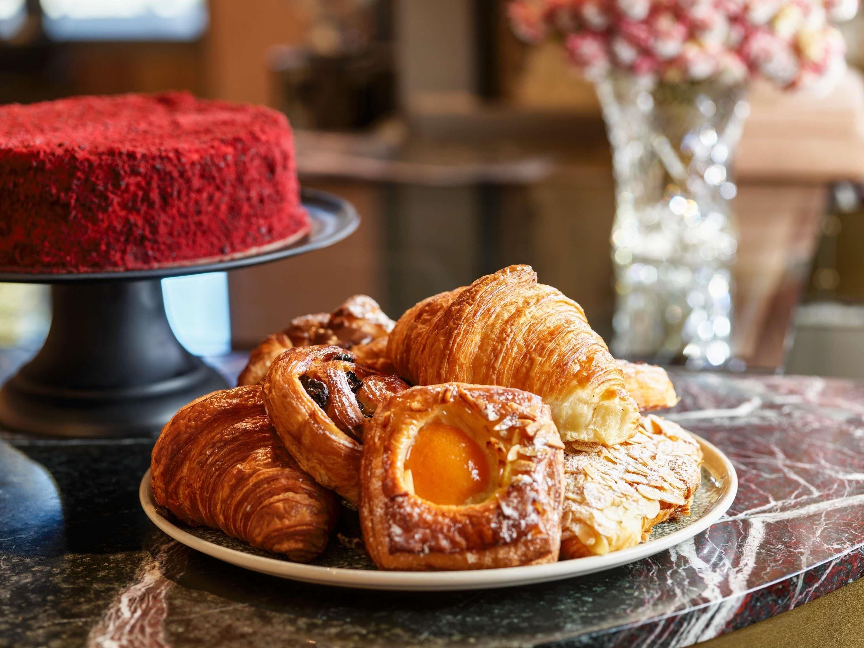 A plate of pastries and a red cake on a marble countertop.
