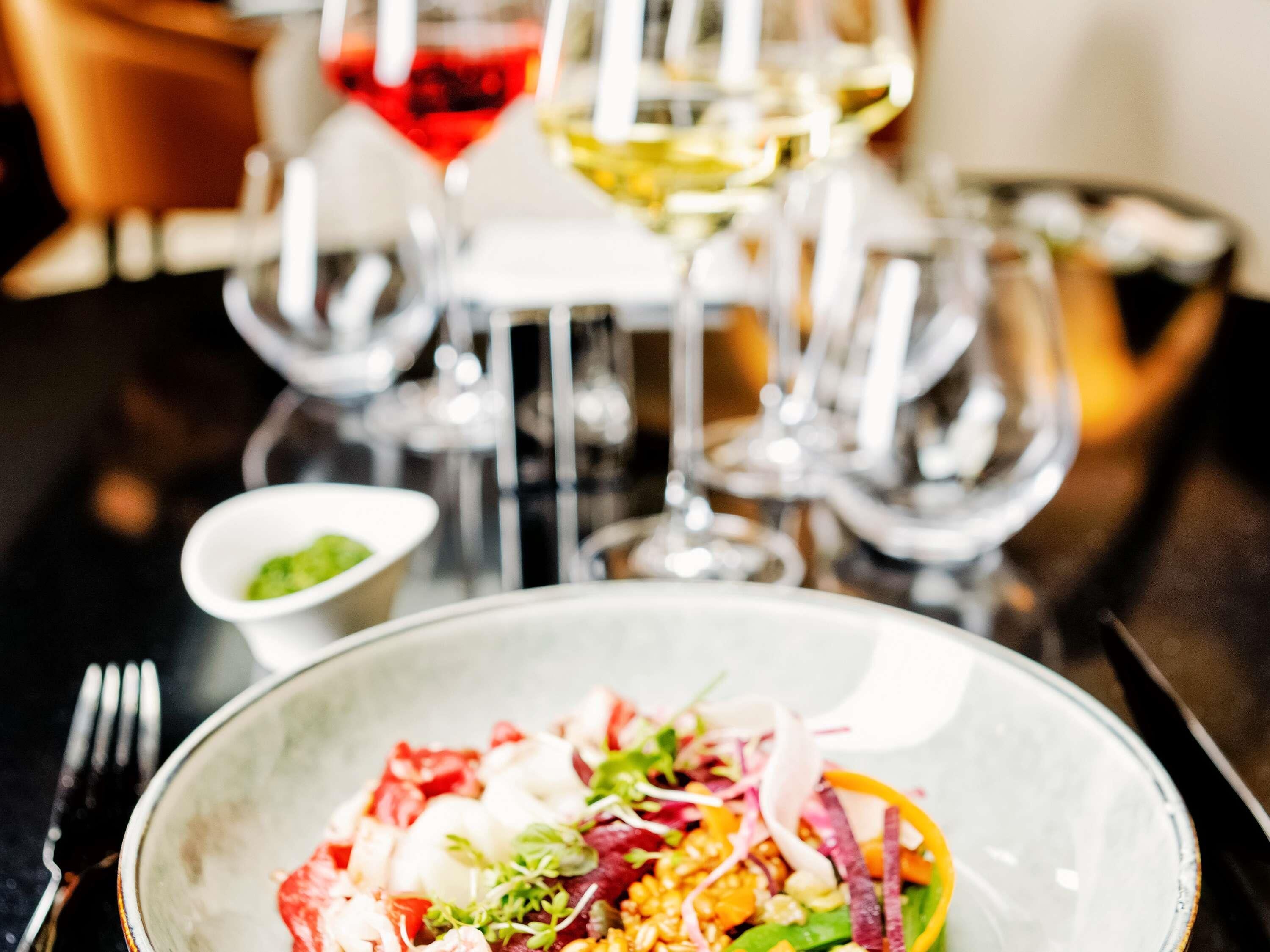 A dining table with a bowl of food, a fork, and multiple wine glasses.