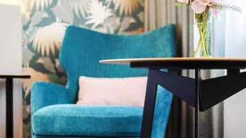 A teal armchair with a white cushion, a small table with a black frame, and a vase with flowers.
