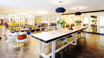 A modern restaurant with a long central bar, multiple seating areas, and contemporary lighting fixtures.