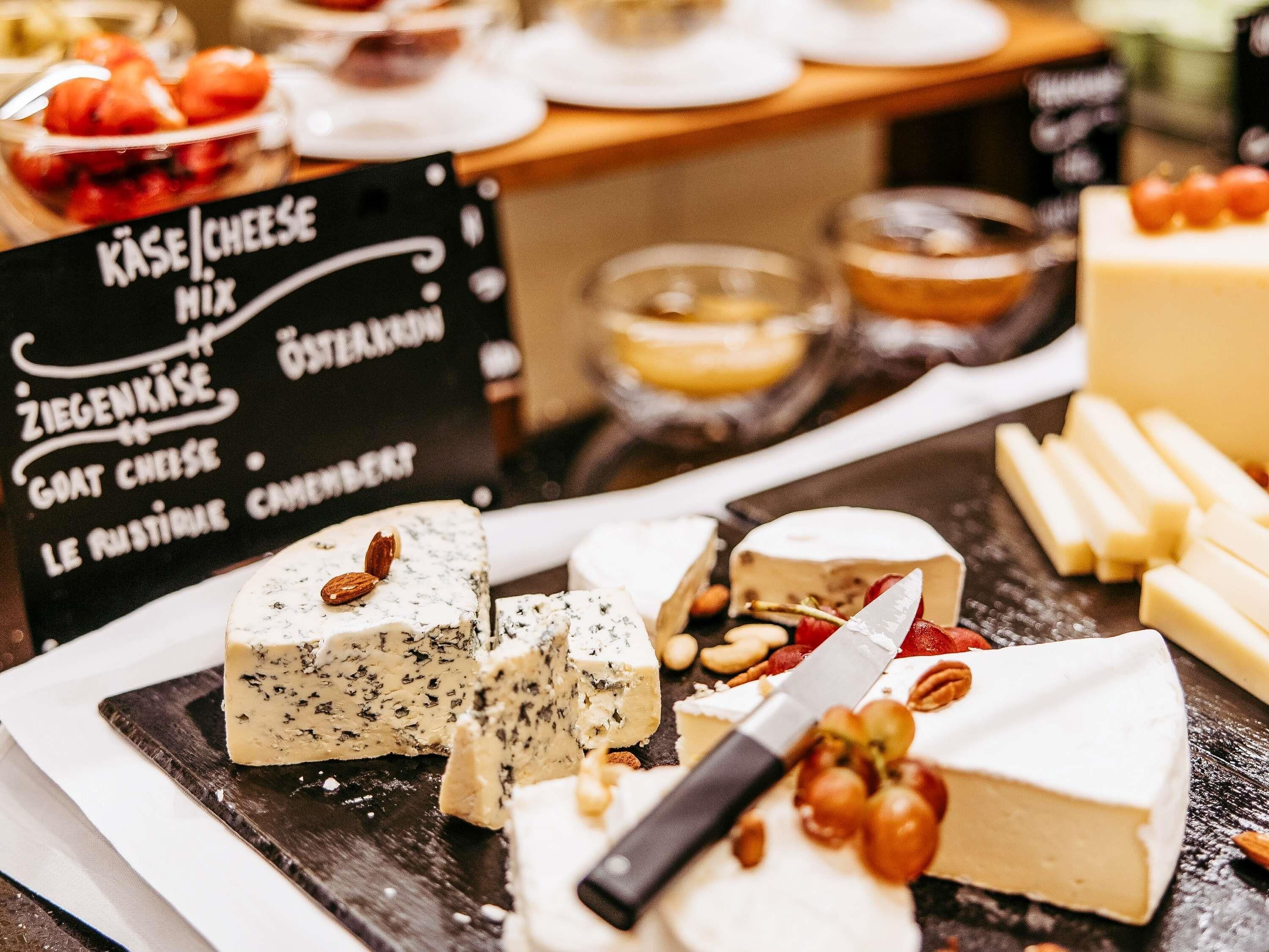 A variety of cheeses displayed on a wooden board with a sign listing types like Ziegenkäse and Goat Cheese.