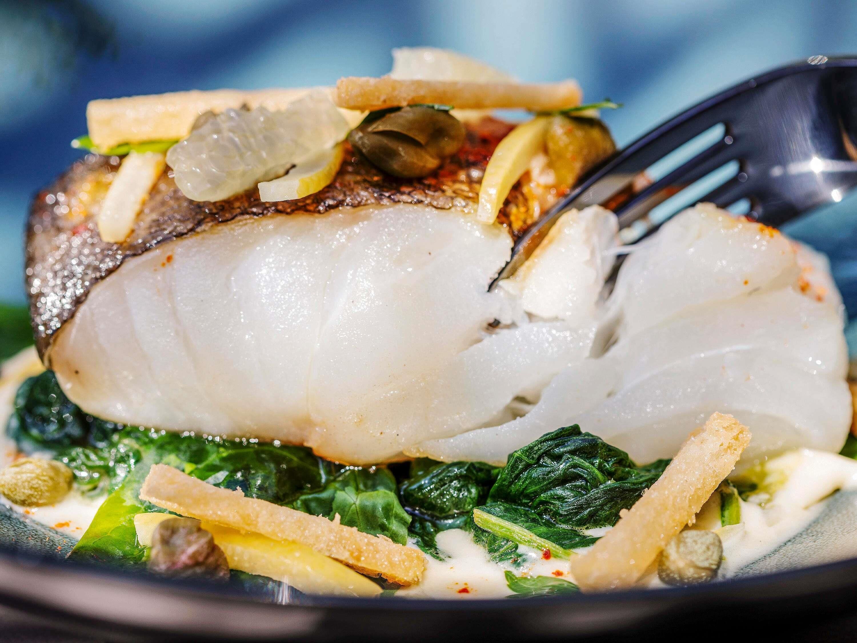 A plate of food with a fish fillet, greens, and some garnishes.