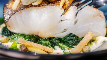 A plate of food with a fish fillet, greens, and some garnishes.