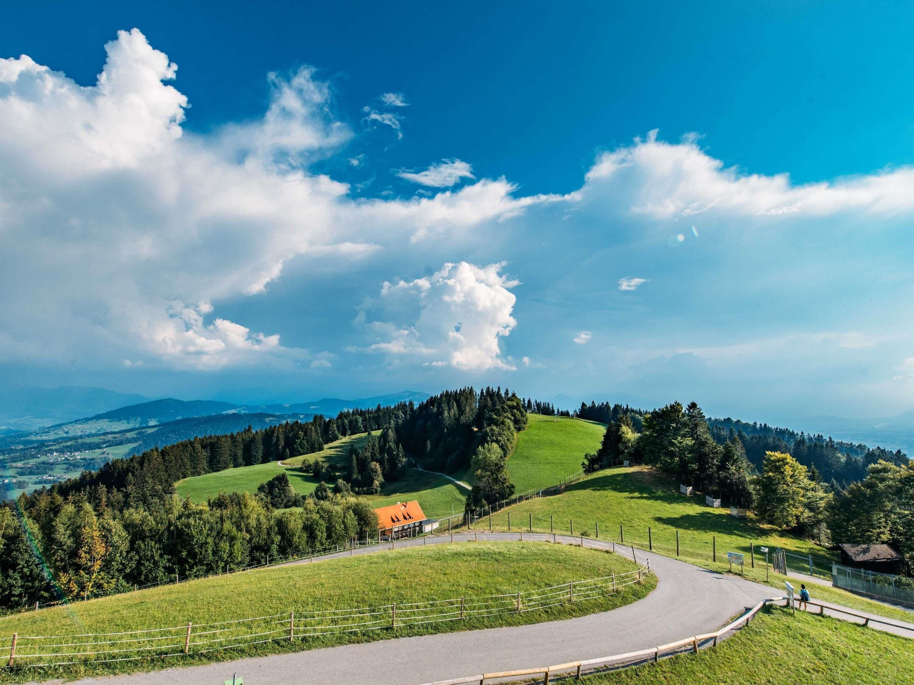 A winding road, green fields, and a building with an orange roof.