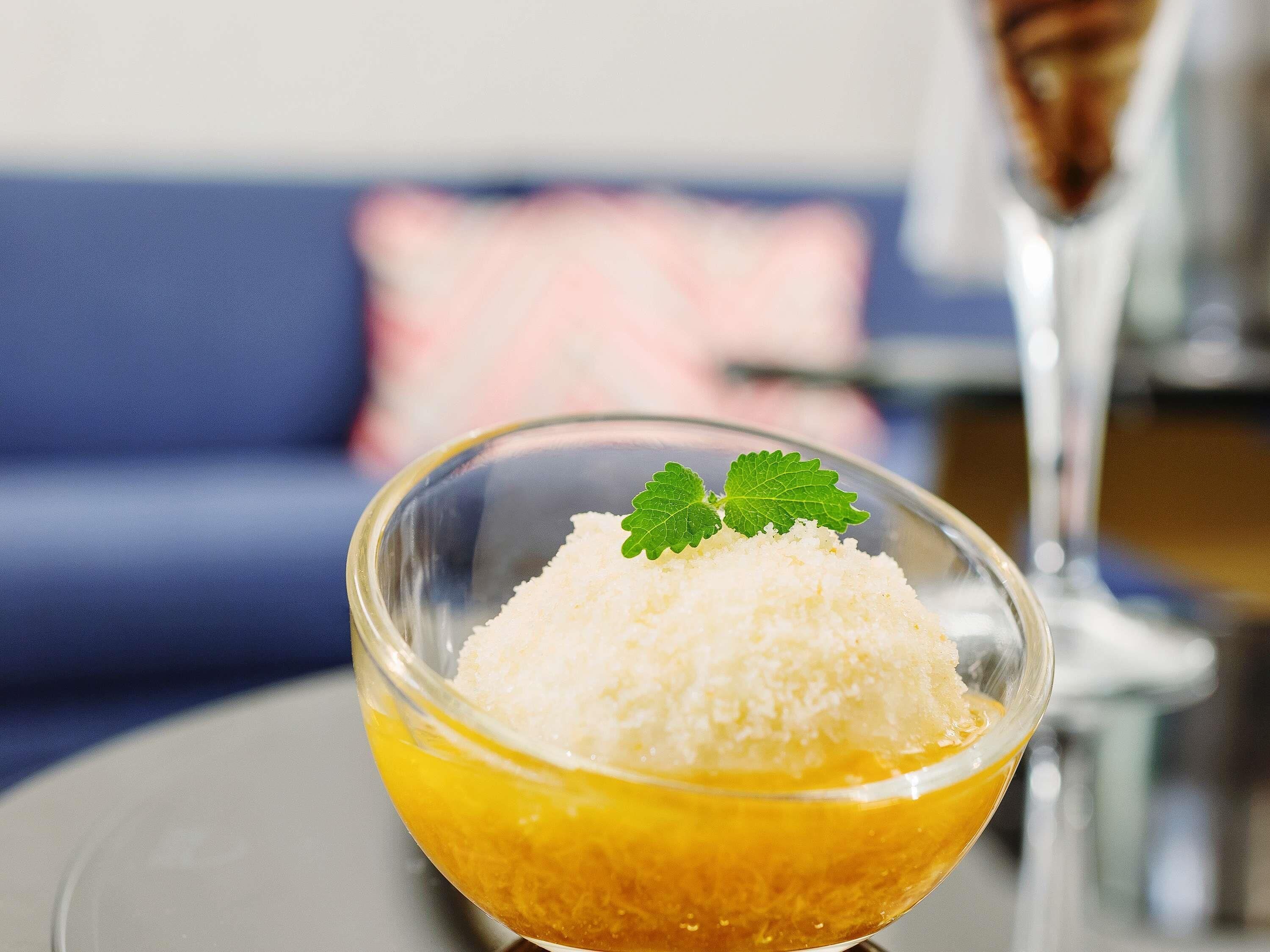 A clear glass bowl with a white granular substance, possibly sugar, on a reflective surface.