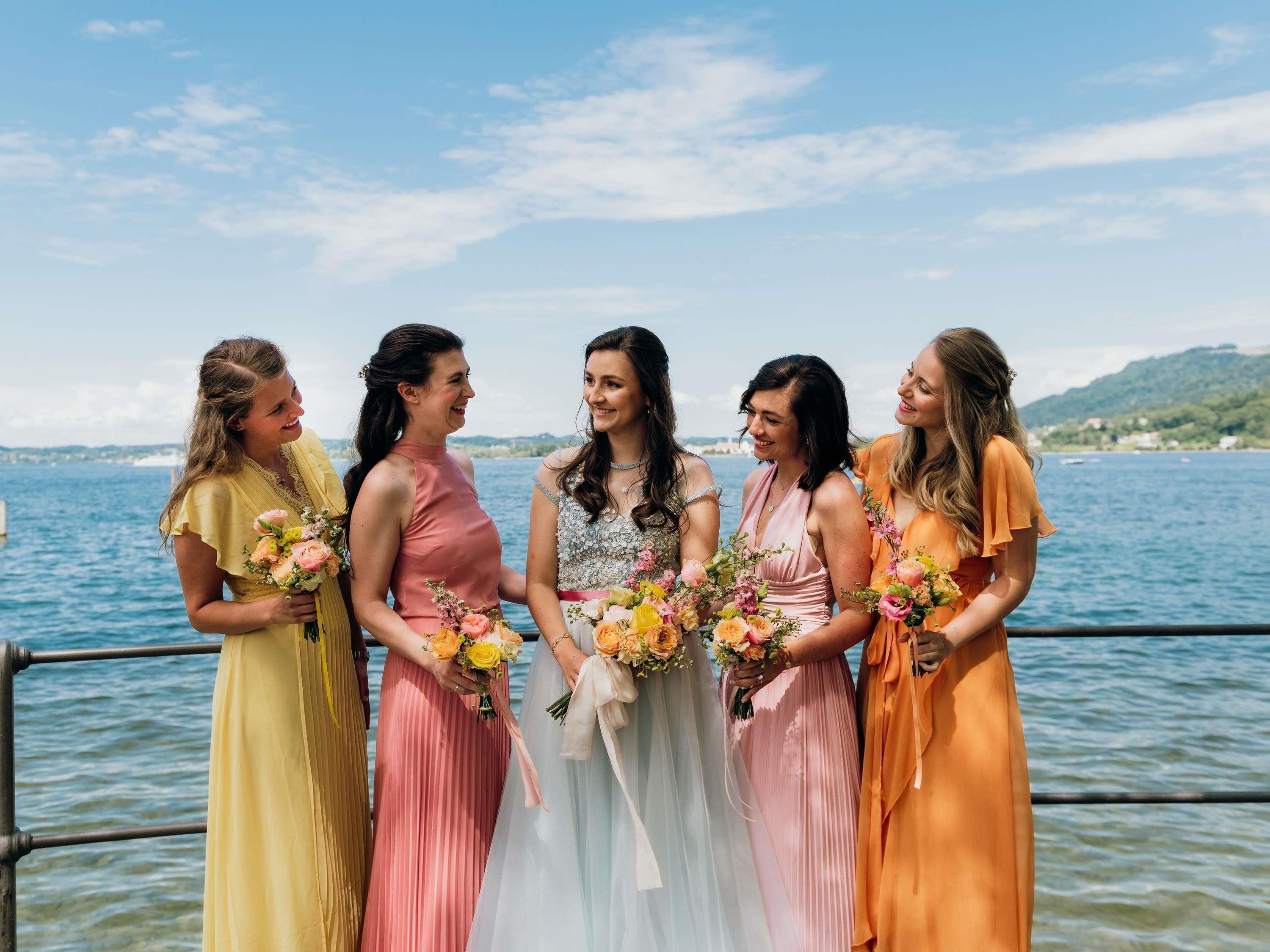 Un groupe de femmes, vêtues de robes colorées, se tient près d’une étendue d’eau, sous un ciel dégagé.