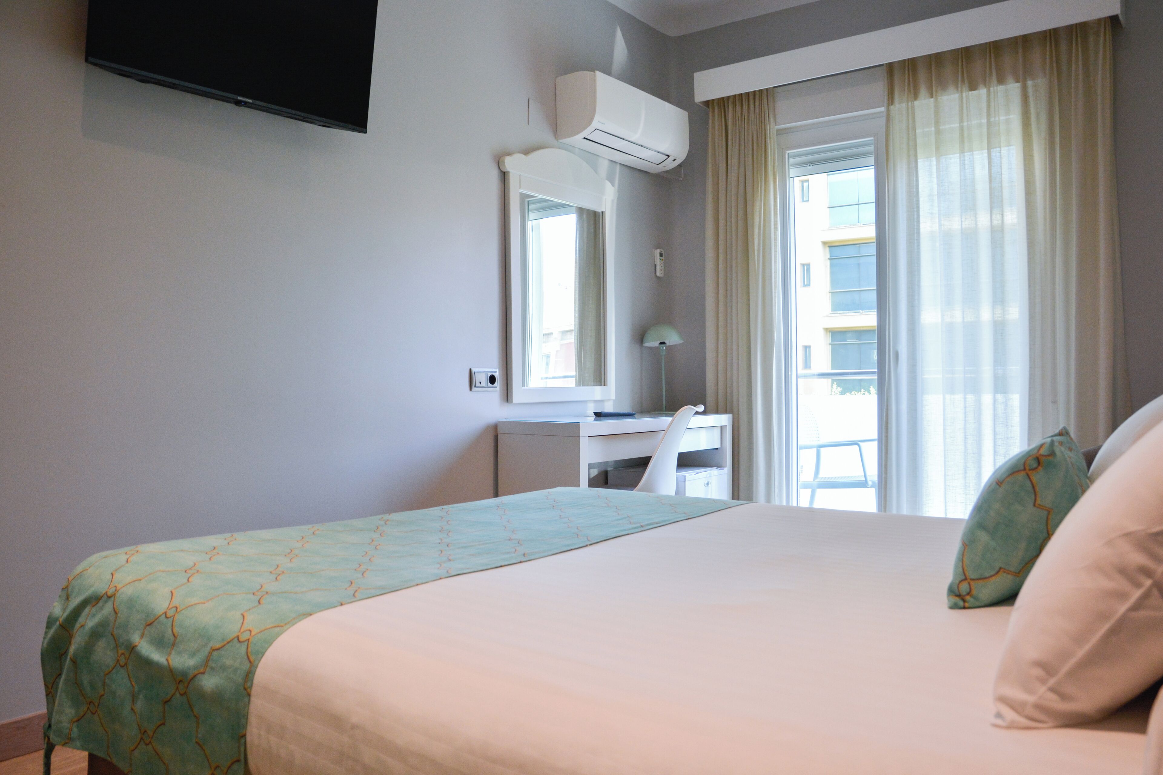 Habitación de hotel con cama, escritorio, silla, televisión y ventana con cortinas.