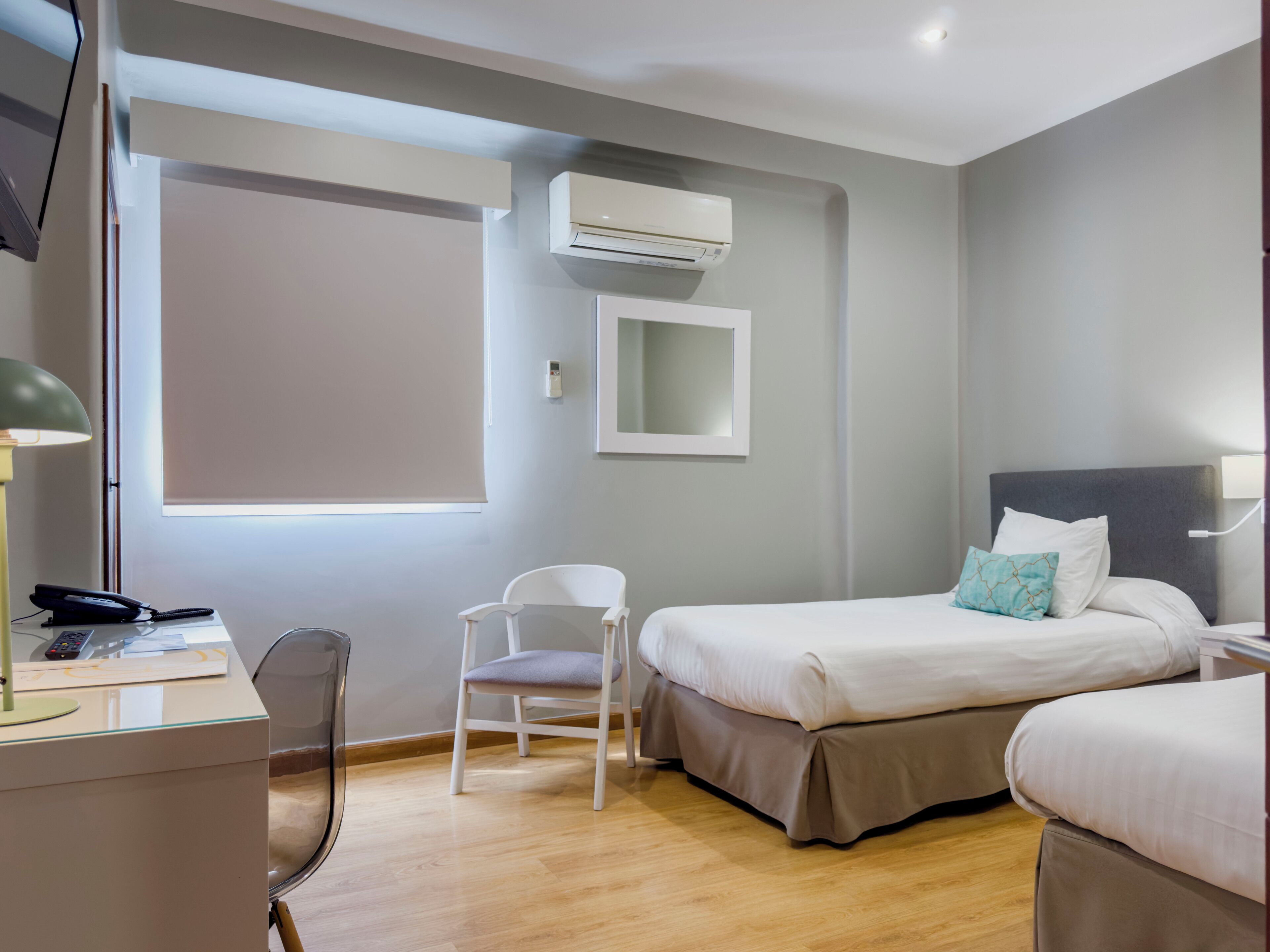 A hotel room with a bed, a desk, a chair, and an air conditioning unit.
