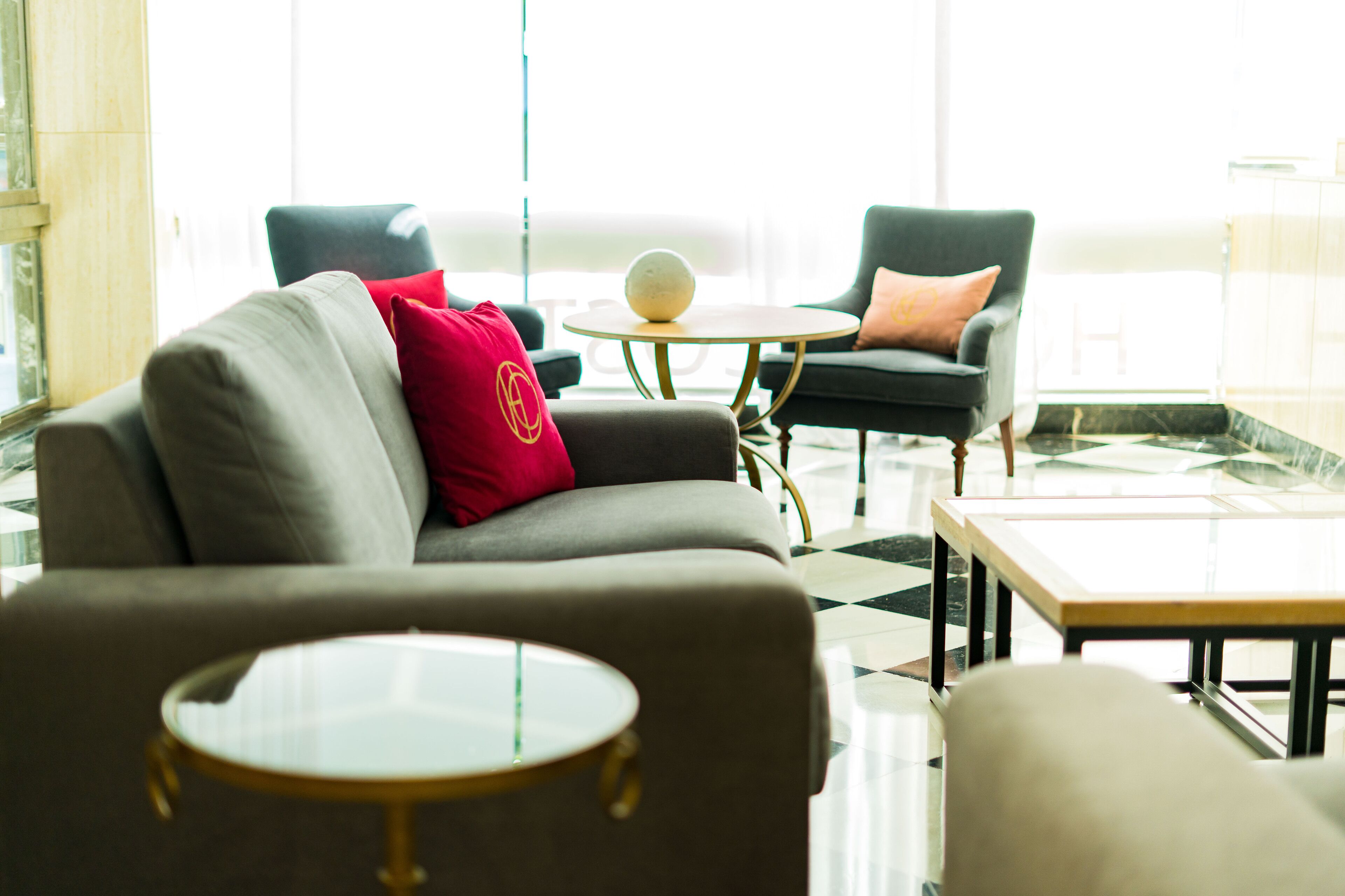 Un vestíbulo moderno con un sofá gris, dos sillones, una mesa redonda y un suelo a cuadros.
