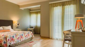 A hotel room with a bed, a desk, a chair, a lamp, and a window with curtains.