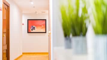 A hallway with a wooden floor, a framed painting on the wall, and a potted plant in the foreground.
