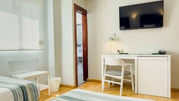 A hotel room with a bed, a desk, a chair, a TV, and a bathroom visible through an open door.