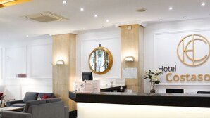 Zona de recepción de hotel con diseño moderno, que incluye un mostrador de recepción, área de estar y un amplio ventanal con marco decorativo.